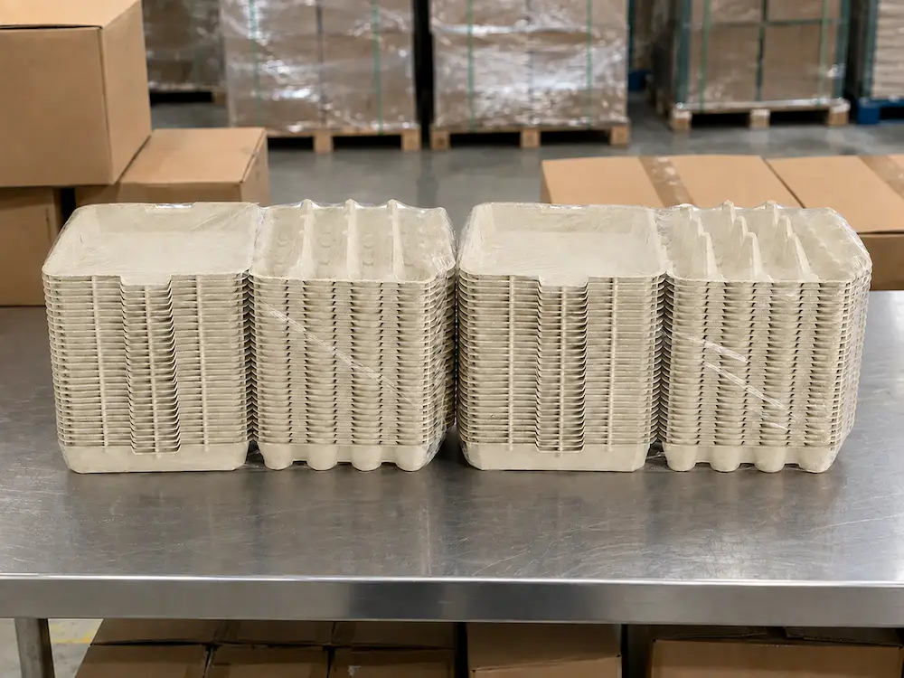 Two PE-wrapped nested stacks of open 20-Count Molded Pulp Egg Cartons with connected lids and egg-cell bases on a factory table