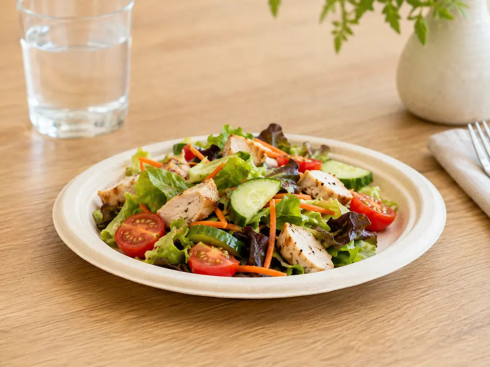 Natural-color 7-Inch Sugarcane Bagasse Round Plate serving grilled chicken salad with mixed greens, cucumber, cherry tomatoes, and carrots