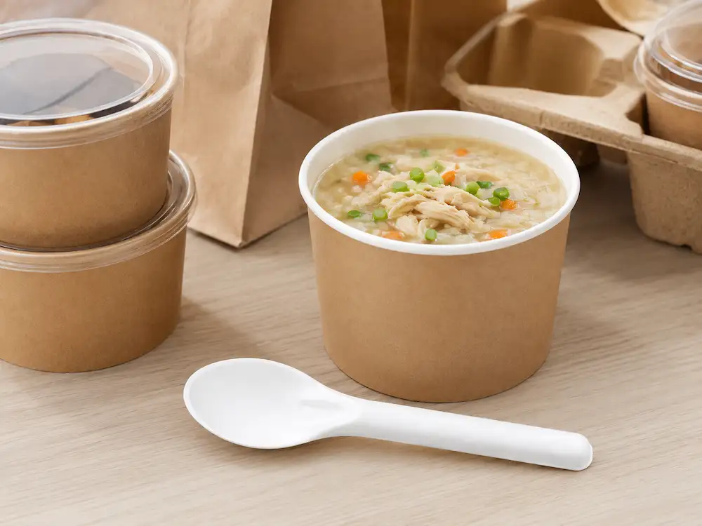 White 6-Inch Wide-Bowl Molded Fiber Spoon beside a takeaway bowl of chicken rice soup in a prepared-meal setting